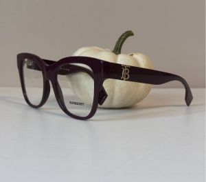 Burberry women’s eyeglasses in deep purple with gold logo detail, displayed with a white pumpkin for a fall theme.